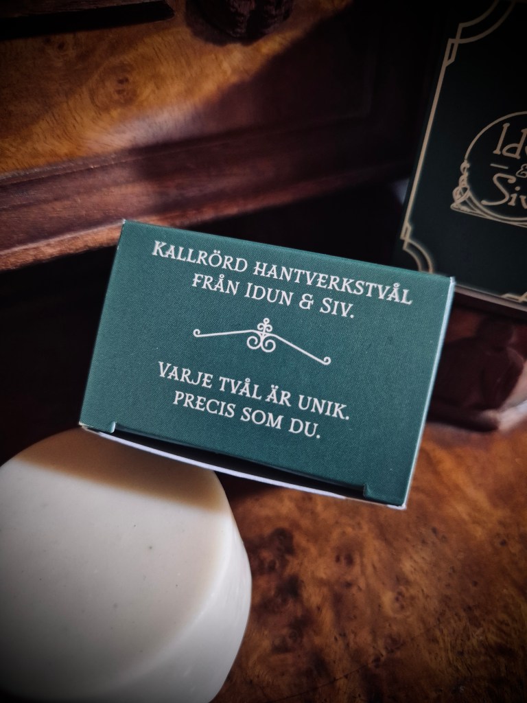 En bild på en tvålask och en vit, rund tvål. På asken står "Kallrörd hantverkstvål från Idun & Siv. Varje tvål är unik. Precis som du."